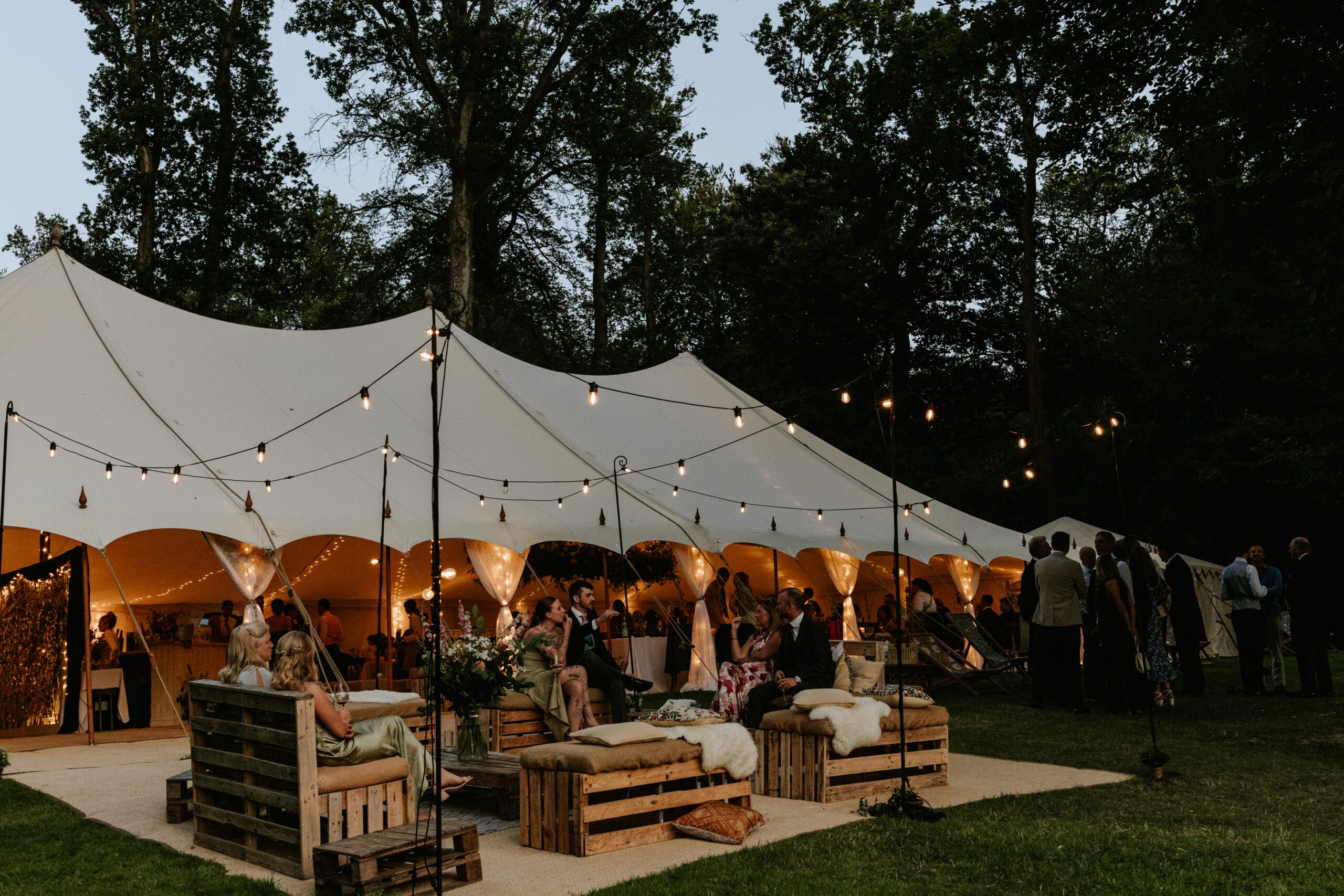 Guests under a stretch tent lit by festoon lights at dusk